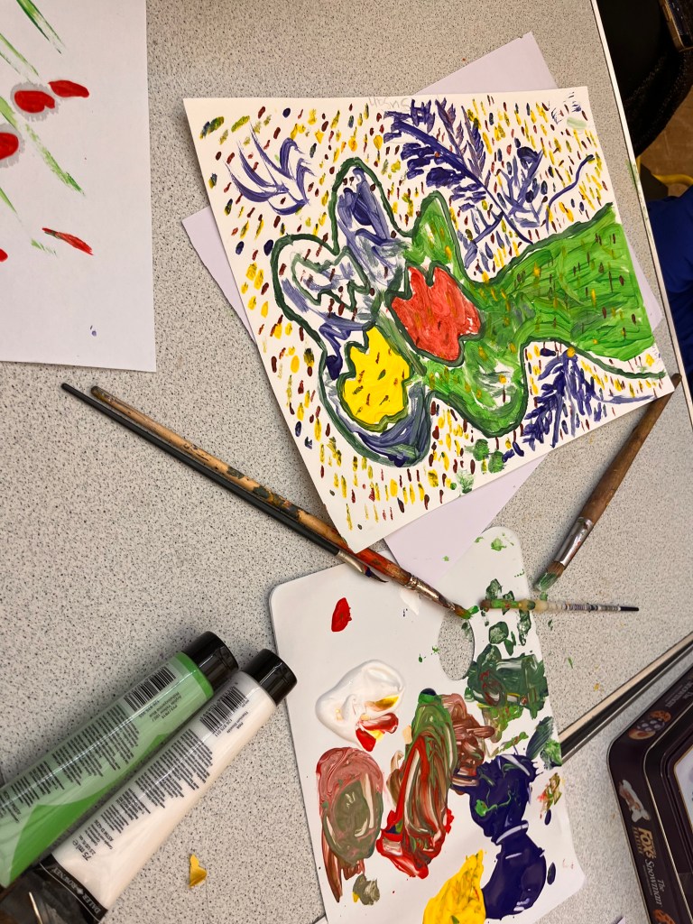 Its a page with multicoloured spots on the paper. Theres blue leaves and then various shapes that are blue, yellow and red- the biggest shape is green.