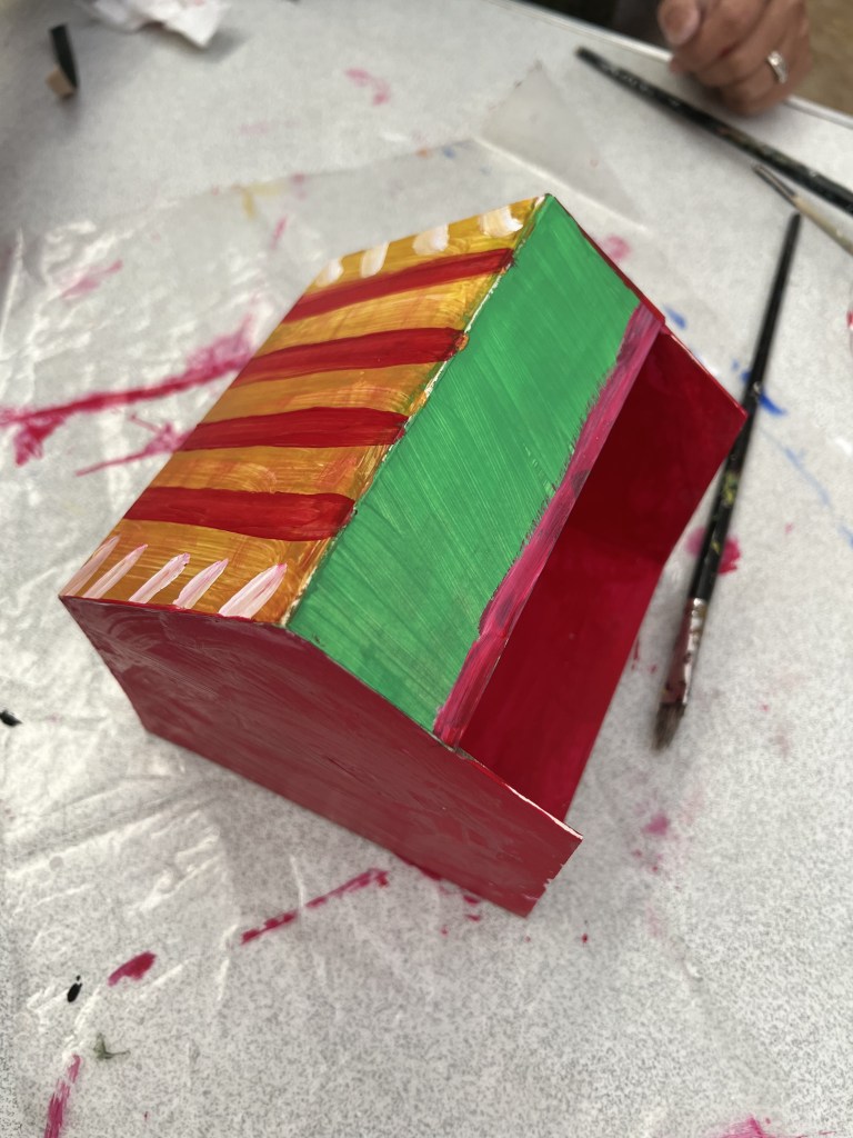 Outside of model house. It has a goldan red sripped roof with a green section. Th walls and floor are painted red.
