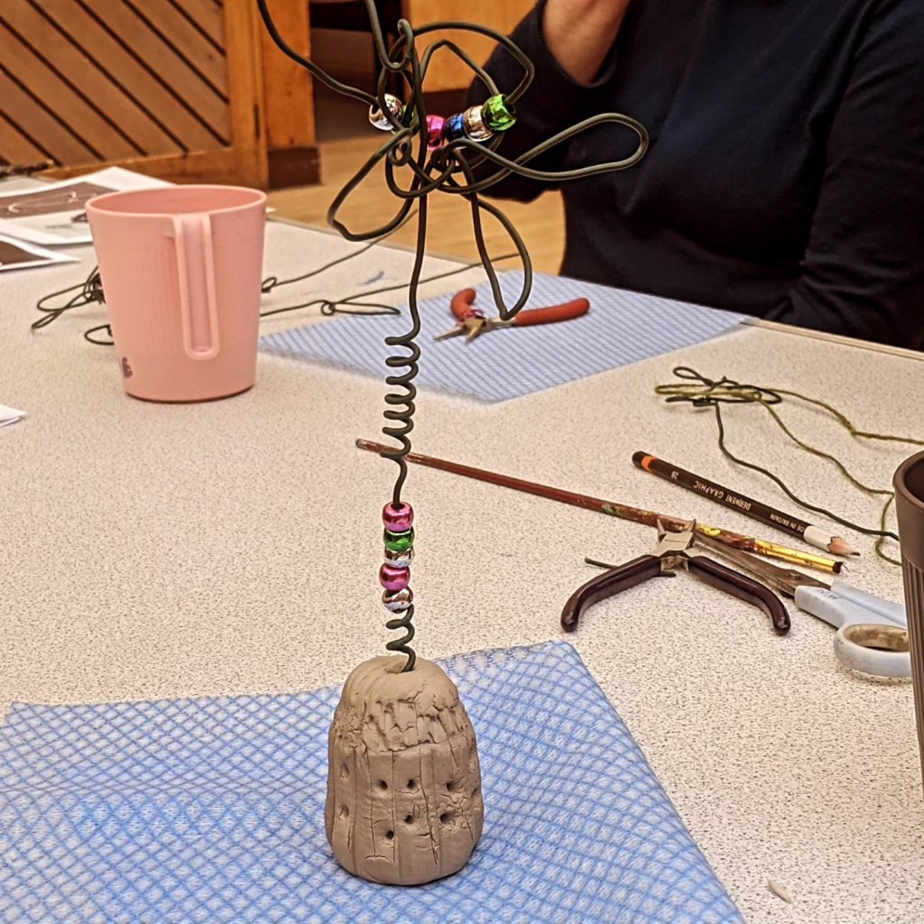 wirework flower standing on a base. There is multicolored beads used throughout the piece.