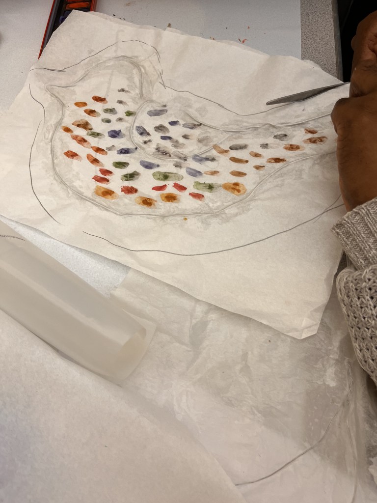 duck wirework piece which is sitting on top of white fabric. the fabric has a tracing of the ducks outline and is being cut into.
The ducks design has orange and blue dotted tones throughout.