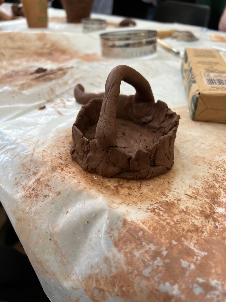 image of clay pot which has a thick base, medium height walls and a rounded handle on the top.