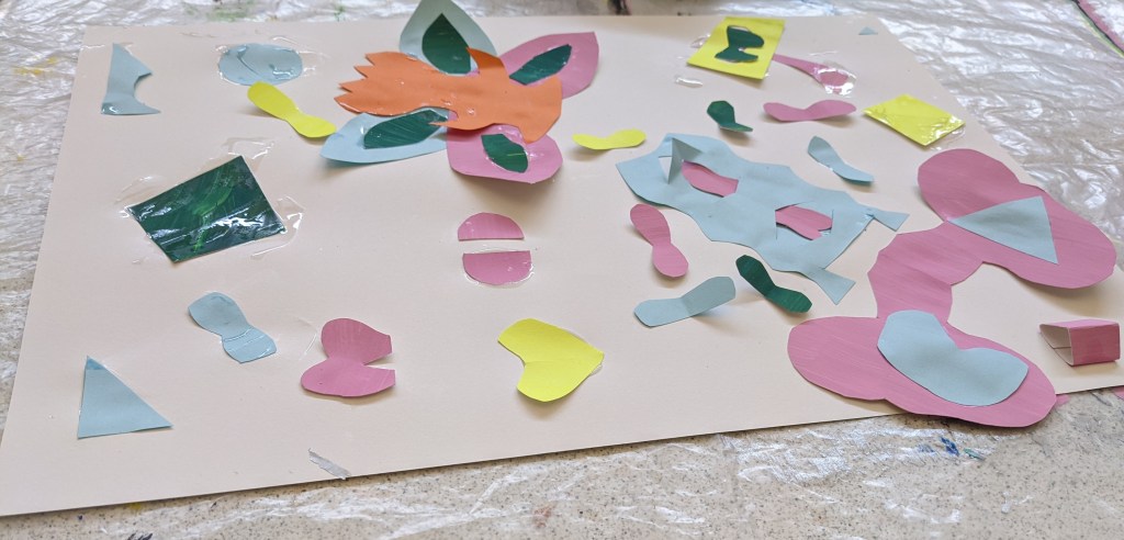 photo of someone arranging blue, pink, yellow and green shapes on page. There are love hearts scattered on page and two pink butterflies.