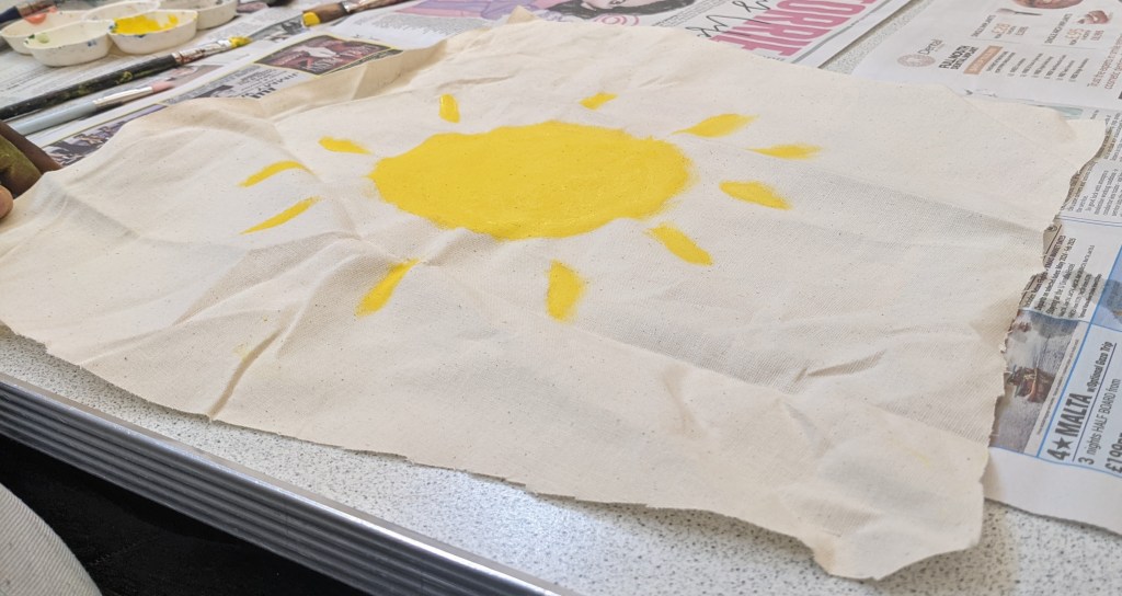 A yellow Sun being painted on a tote bag.