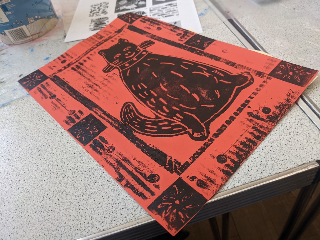 Black cat on orange paper surrounded by a black patterned border.