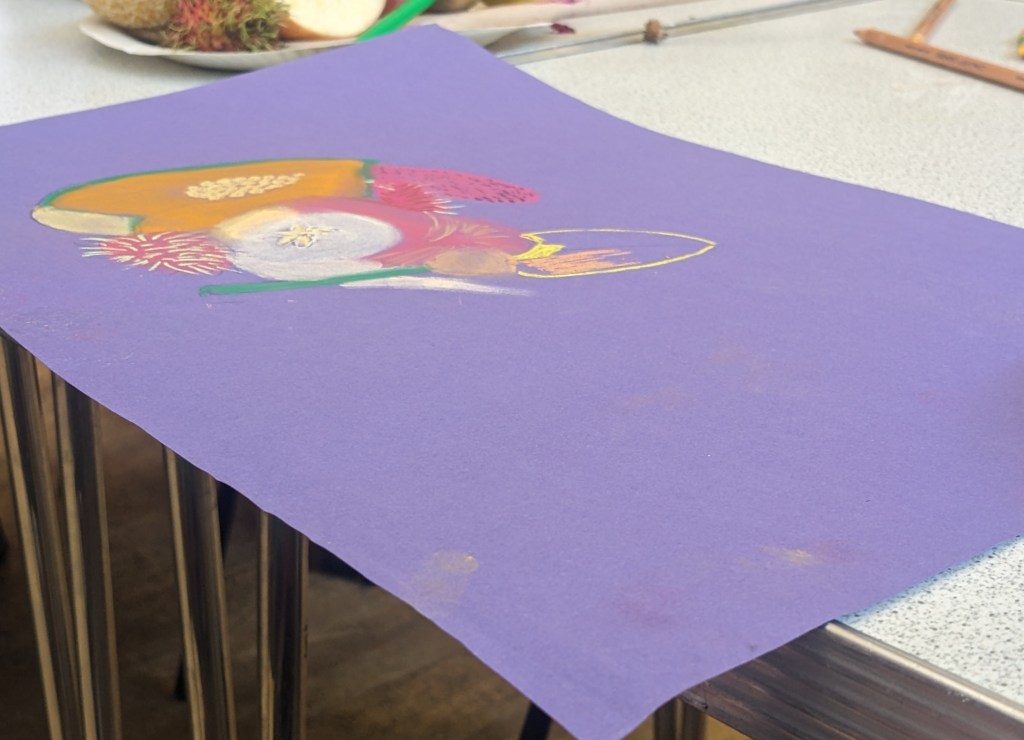 Still life in fruit on purple paper. Fruits are coloured in using pastels.