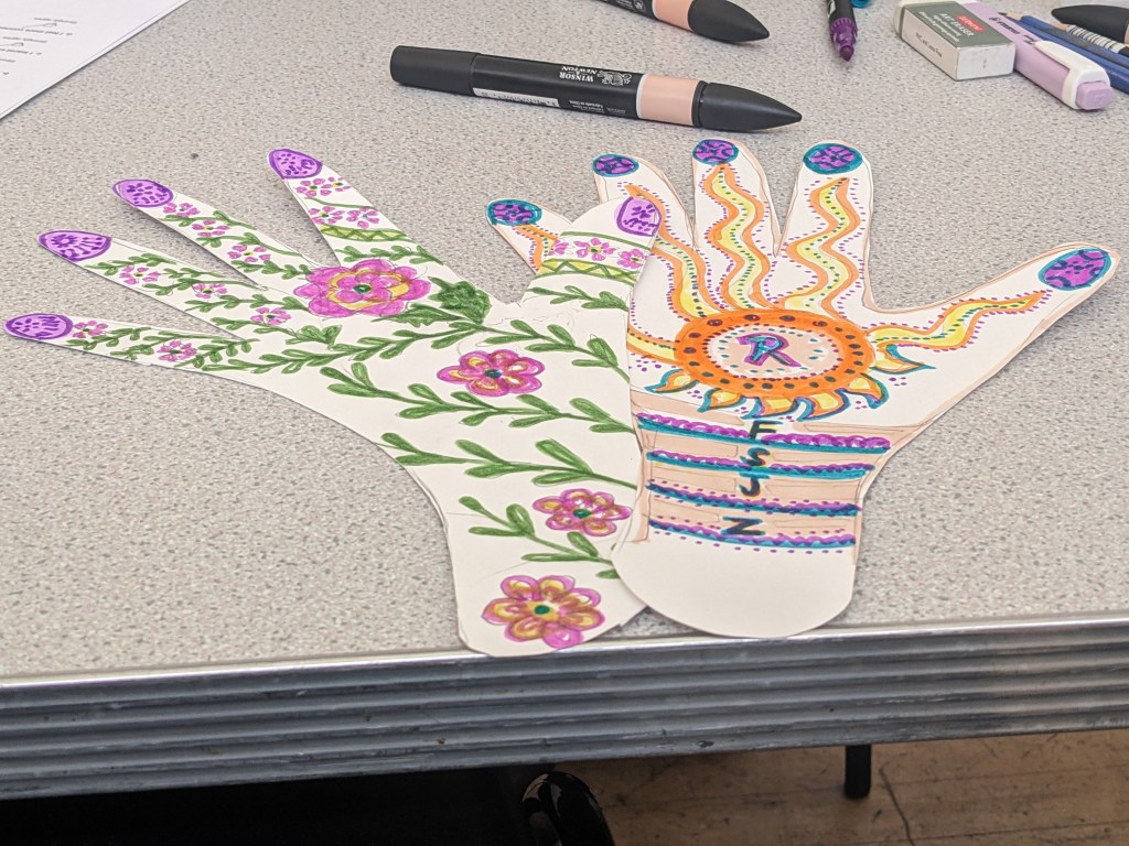 Two paper hands cut out. Both have floral patterns on one is pink the other has more purple, yellow and orange.