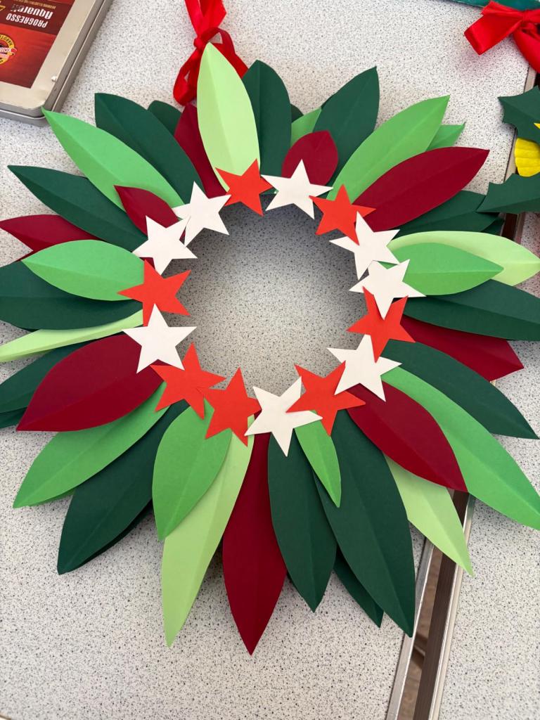 Christmas wreath 1: Has layers of green, dark green and red leaves with red and white stars in the middle in a circle.