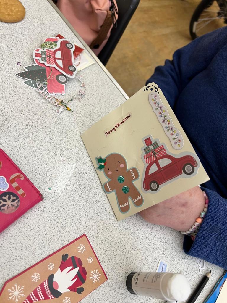 Yellow christmas card saying Merry Christmas. Theres a gingerbread man and a car with presents on the roof side by side on the card.