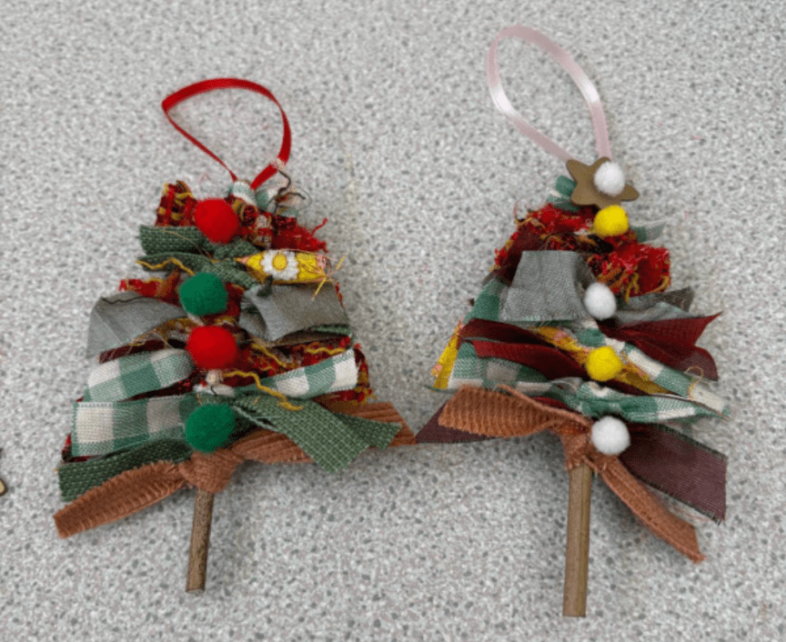 Two Christmas trees made out of fabric scraps. One has red ribbon and red and green fabric balls on. The other has light pink ribbon and yellow and white fabric balls on.