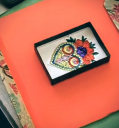 Heart Shrine Box 2: It has a red base and black box on top. In the black box is a red Poppy with multiple leaves. At the bottom us a patterned multicoloured hear with white gems around it. 